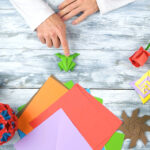 Man at origami folding lesson. Man pointing at origami frog with finger. Collection of beautiful origami figurines on wooden table. Traditional origami paper folding.
