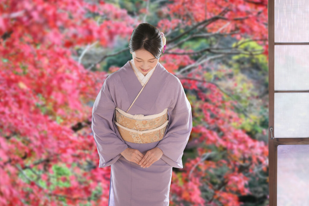 Japanese woman in kimono bowing against a background of autumn leaves Image of Japanese tourism and travel hospitality