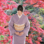 Japanese woman in kimono bowing against a background of autumn leaves Image of Japanese tourism and travel hospitality